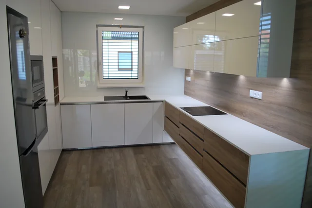 Kuchyň do U s bílými lesklými dvířky, dřevěným obkladem a světlou deskou