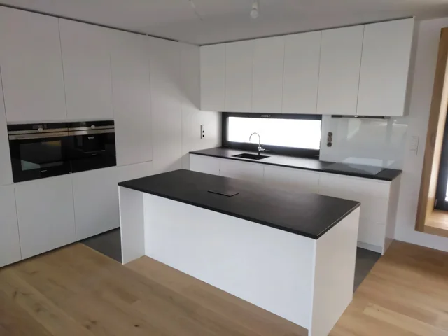 Bílá kuchyň s tmavou deskou a pásovým oknem nad linkou