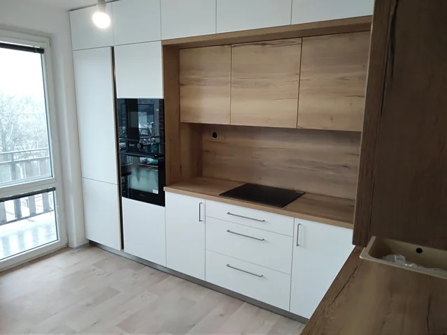 Bílá kuchyň s dřevěným obkladem a vysokým oknem u linky