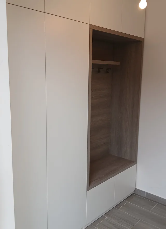 Bílá vestavěná skříň s dřevěným výklenkem na kabáty